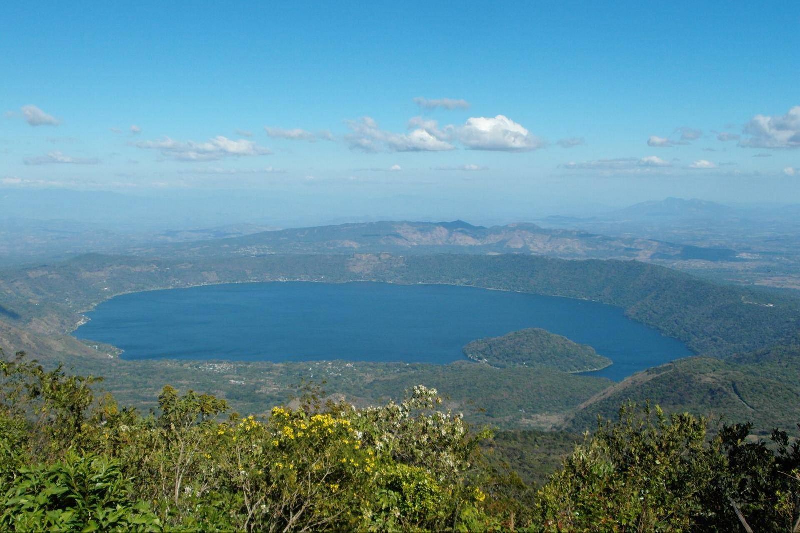 Lago de Coatepeque visto desde lo alto, con flores amarillas en primer plano